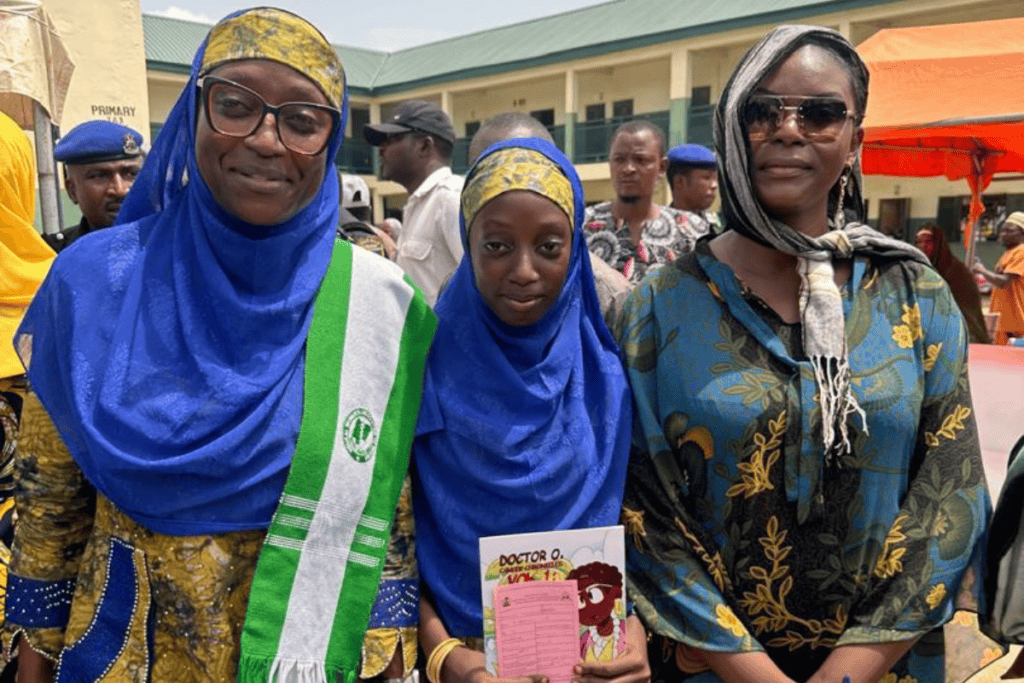Elizabeth Hassan and a parent with eligible child showing vaccination card and comic book (gift).