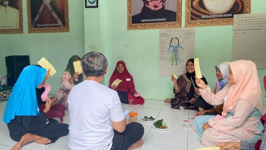a group of indonesian mothers sit in a circle together holding up pieces of paper