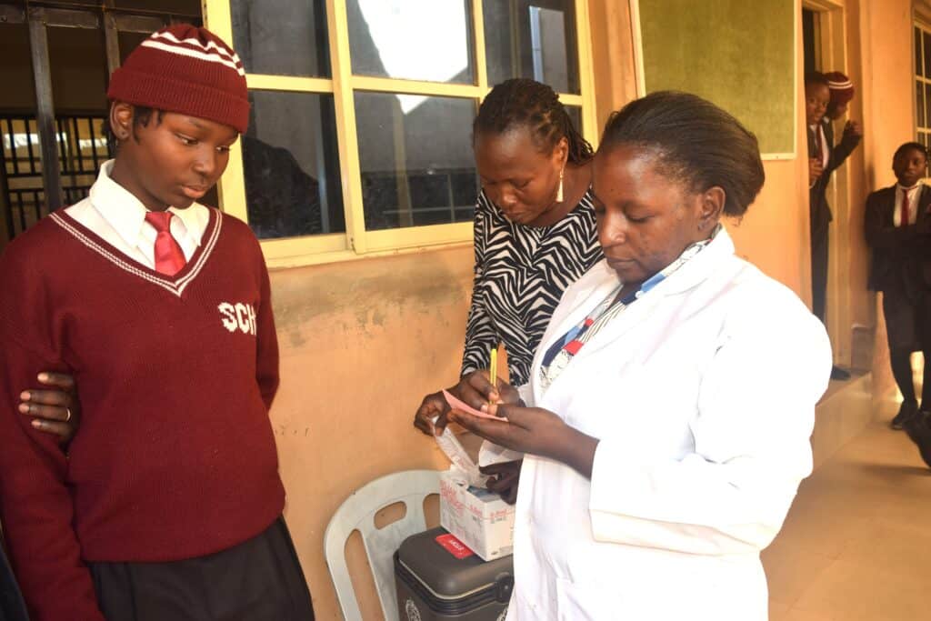 A nurse fills out a vaccination card while two students stand at her side.