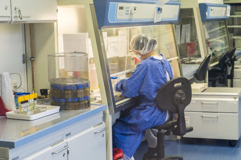 A lab worker works at a station in a lab wearing protective equipment