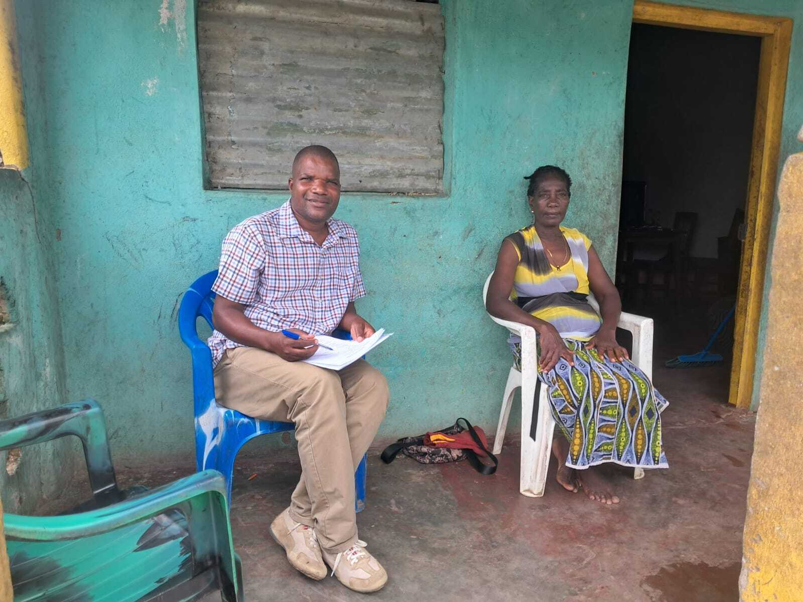 A man sits in a village in Mozambique interviewing a woman who is sitting with him.
