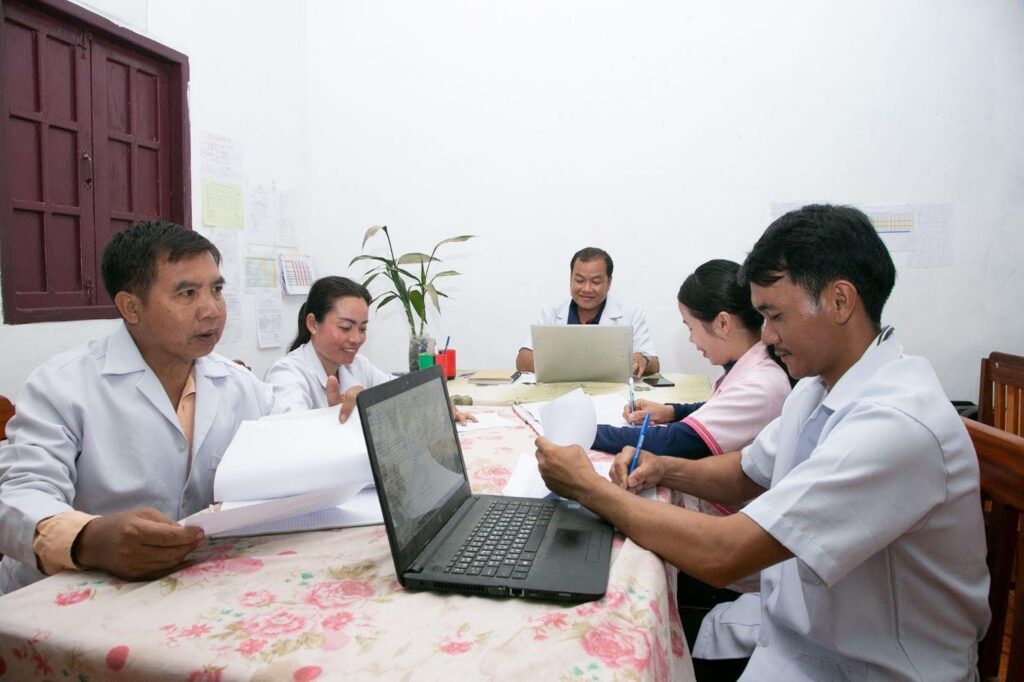 A group of adults work around a table on laptops in Laos