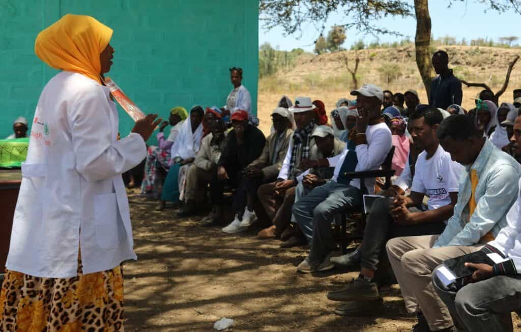 A woman presents to a group of people during an outdoors meeting in Ethiopia.