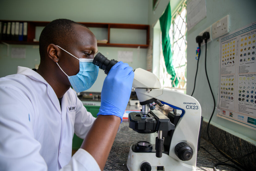A lab technician in Uganda looks in a microscope.