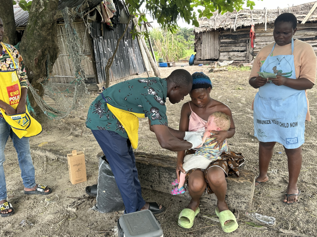 A Nigerian mother holds her baby in a village while the baby receives an immunization.