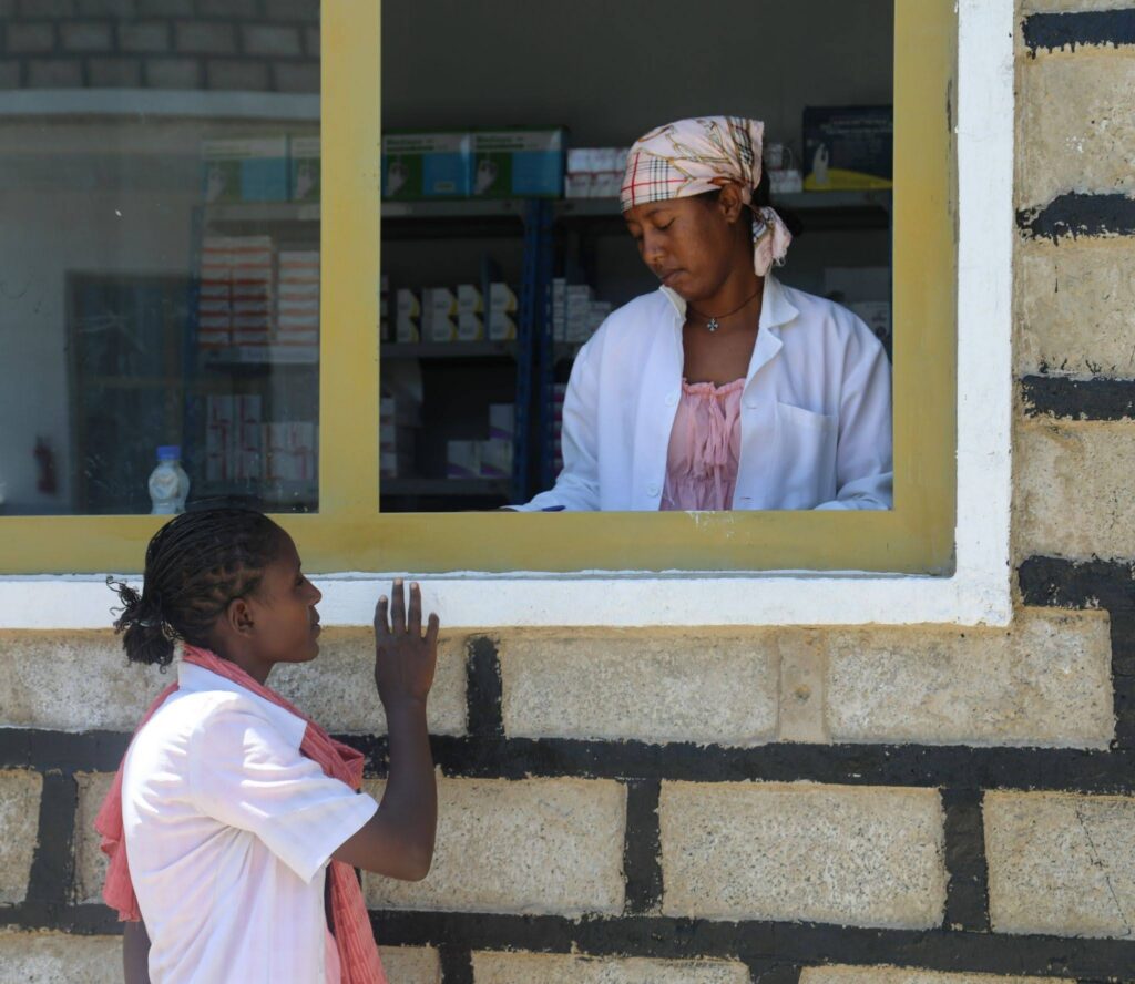 A woman stands at a pharmacy window in Ethiopia speaking with a pharmacist.