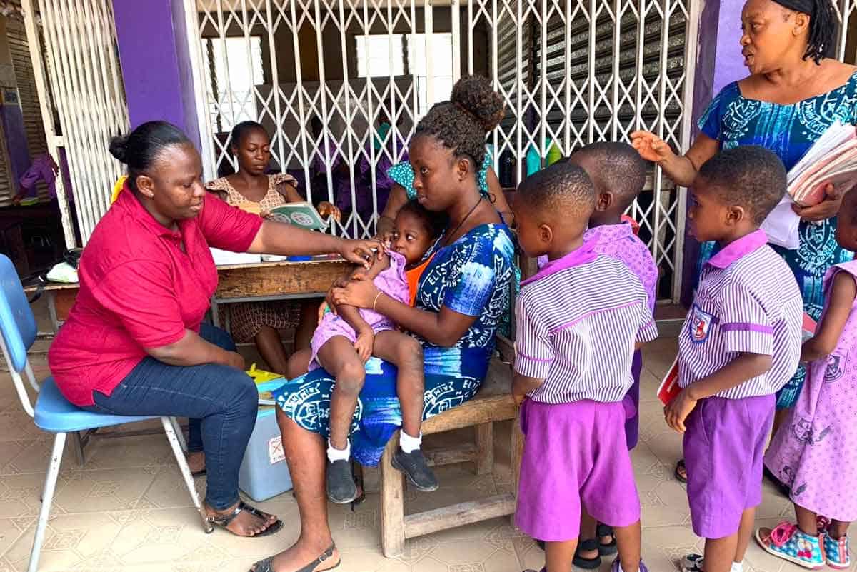 A health care worker (left, in red) administers a vaccine to a child at a nursery school in Ashaiman, Ghana.