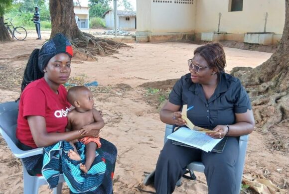 A mother holds a child and sits with a health worker outside in a village in Mozambique