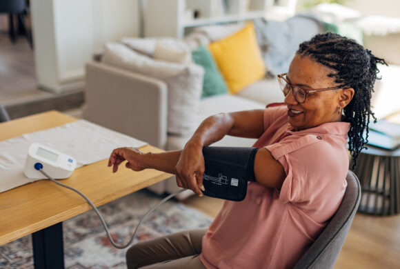 Mature black woman monitoring heart health with arm cuff at dining table