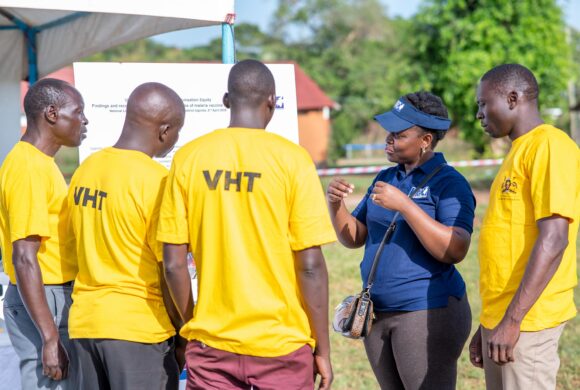 A group of adults meet outside in Uganda and are discussing.