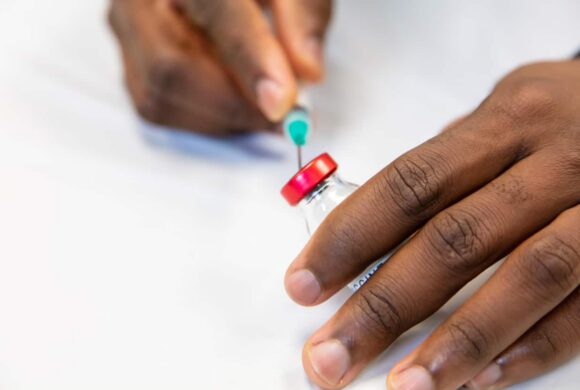 A close up image of hands drawing a vaccine from a vial to a syringe.