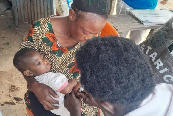A baby being held by its mother is vaccinated in Nigeria by a health care worker.