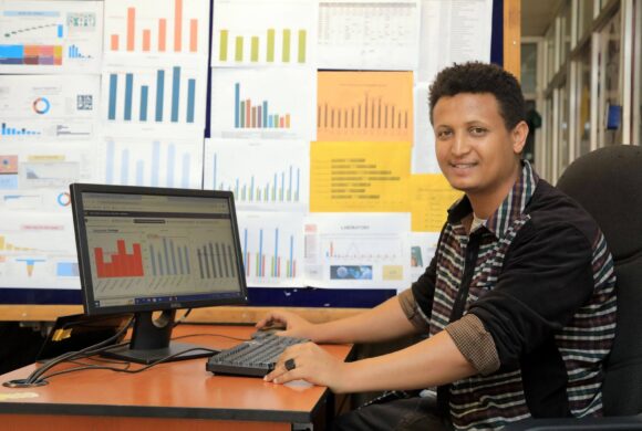 A person sits at a desk smiling for the camera with a laptop in front of them.