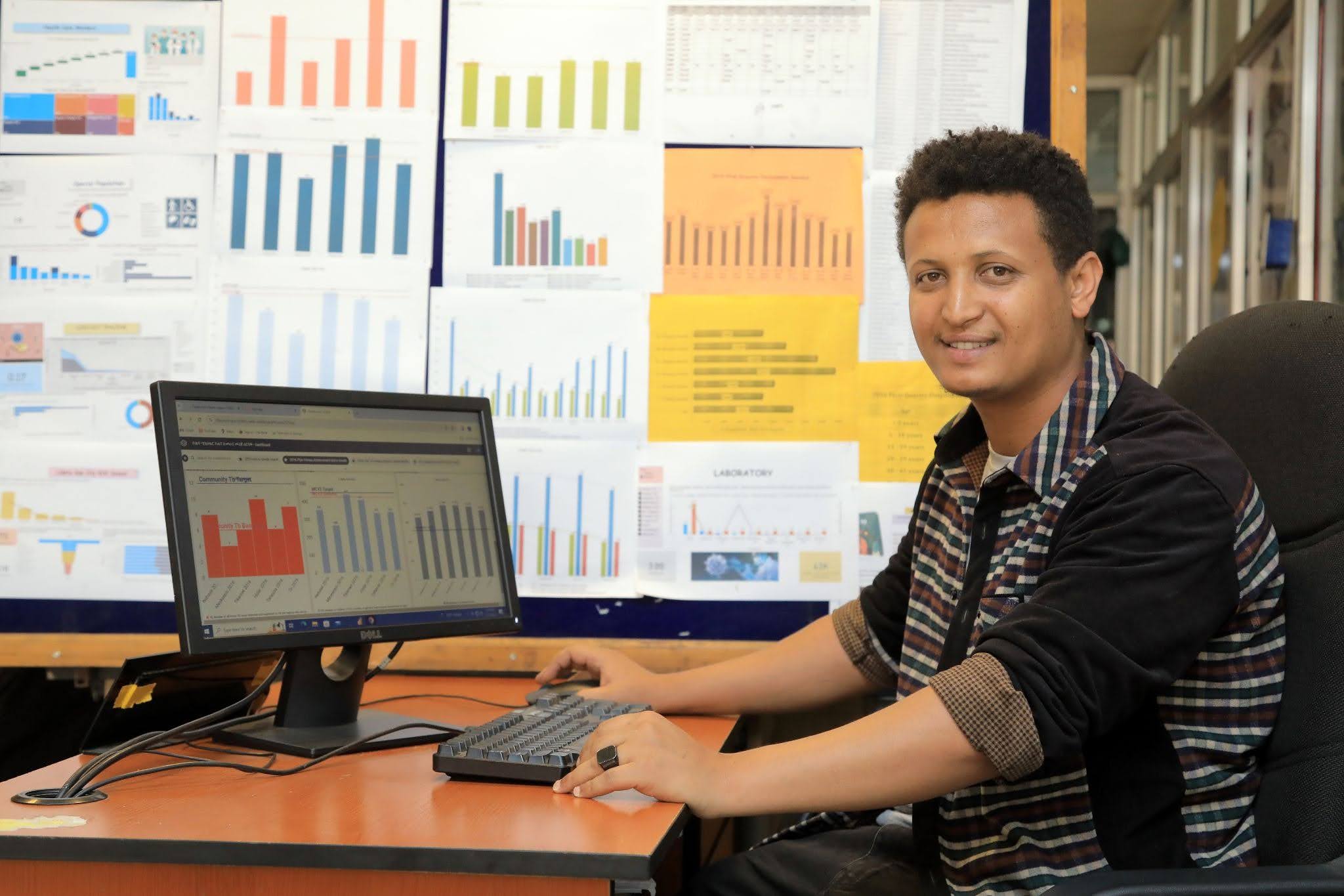 A person sits at a desk smiling for the camera with a laptop in front of them.
