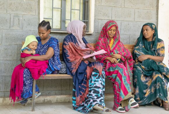 A group of Ethiopian mothers sit outside a clinic together.