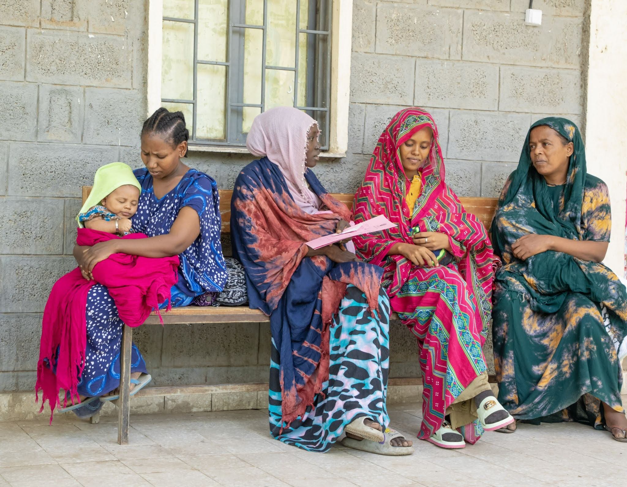 A group of Ethiopian mothers sit outside a clinic together.
